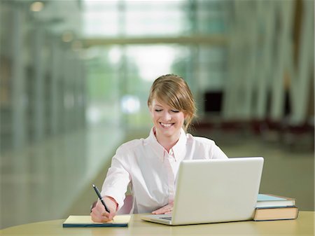 studying (university age) - Young student studying taking notes and using laptop, smiling Stock Photo - Premium Royalty-Free, Code: 614-06895708