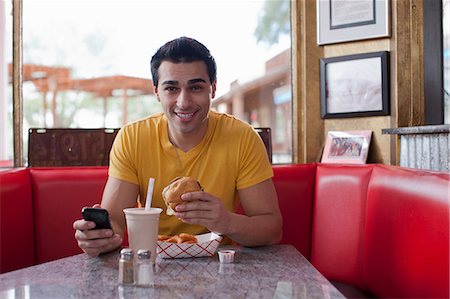 diner - Young man texting on mobile phone and eating fast food in diner, portrait Stock Photo - Premium Royalty-Free, Code: 614-06896134