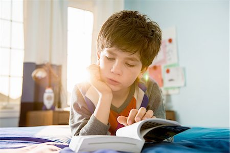 Boy lying on bed reading book Stock Photo - Premium Royalty-Free, Code: 614-06897712