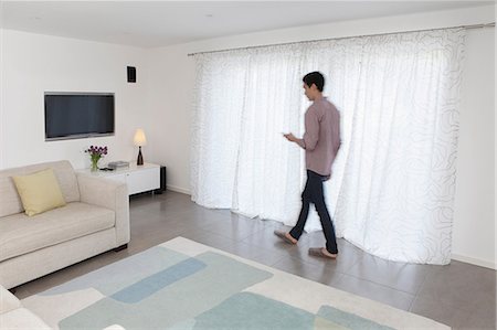 people home comfort adult - Man with mobile phone walking past curtains Stock Photo - Premium Royalty-Free, Code: 614-06898611