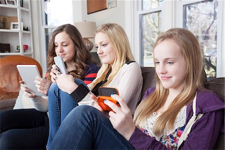 Girls sitting on sofa using digital tablet, cellular telephone and handheld video game Stock Photo - Premium Royalty-Free, Code: 614-06974315