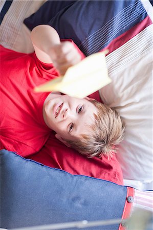 Boy on bed playing with paper aeroplane Stock Photo - Premium Royalty-Free, Code: 614-06973566