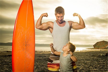 surfboard beach - Young man and son flexing muscles on beach Stock Photo - Premium Royalty-Free, Code: 614-07031183