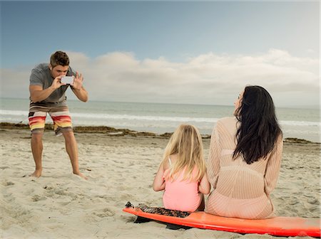 Man photographing family as the sit on a surfboard Stock Photo - Premium Royalty-Free, Code: 614-07031190