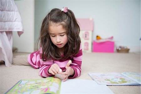 Girl lying on front and reading sticker book Stock Photo - Premium Royalty-Free, Code: 614-07032016