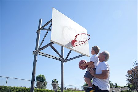 family outdoors blue sky - Man lifting grandson to basketball hoop Stock Photo - Premium Royalty-Free, Code: 614-07146504