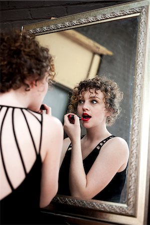 Portrait of young woman applying lipstick in mirror Stock Photo - Premium Royalty-Free, Code: 614-07240101