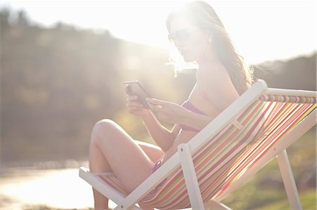 phone summer - Young woman on deckchair texting from cellphone Stock Photo - Premium Royalty-Free, Code: 614-07444302