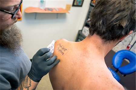 stenciling - Tattooist marking out "my first tattoo" on customer's shoulder Stock Photo - Premium Royalty-Free, Code: 614-07735142