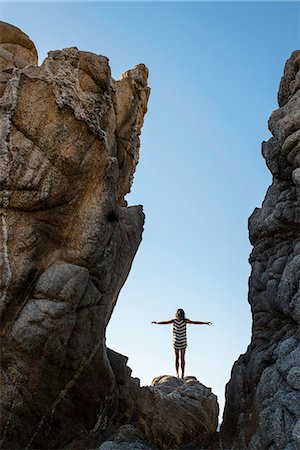 Young woman standing on rocks on beach, arms outstretched Stock Photo - Premium Royalty-Free, Code: 614-07768258