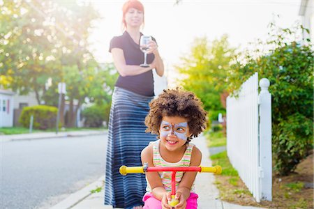 Girl with painted face crouching on scooter on suburban street Stock Photo - Premium Royalty-Free, Code: 614-07805730