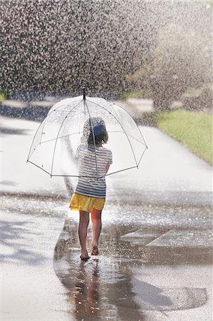 sunny street - Rear view of barefoot girl carrying umbrella walking through street puddle Stock Photo - Premium Royalty-Free, Code: 614-07806399