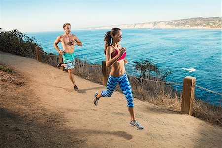 Mid adult man and young woman running on path by sea Stock Photo - Premium Royalty-Free, Code: 614-07912034