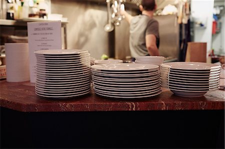 simsearch:630-06723923,k - Plates stacked on counter in restaurant, restaurant worker in background Stock Photo - Premium Royalty-Free, Code: 614-08030794