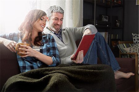 Young couple sitting on sofa drinking coffee and looking at digital tablet Stock Photo - Premium Royalty-Free, Code: 614-08065899