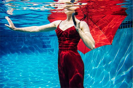 Mature woman wearing red dress, holding red umbrella, underwater view, mid section Stock Photo - Premium Royalty-Free, Code: 614-08065890