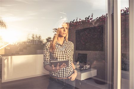 pensive - Portrait of young woman with digital tablet gazing from suburban window Stock Photo - Premium Royalty-Free, Code: 614-08081432