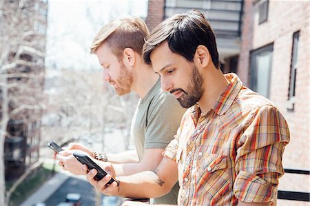 simsearch:614-08148673,k - Male couple standing on balcony, looking at smartphones Stock Photo - Premium Royalty-Free, Code: 614-08148677
