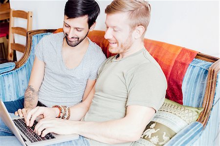 simsearch:614-08148673,k - Male couple sitting on sofa, looking at laptop, smiling Stock Photo - Premium Royalty-Free, Code: 614-08148690