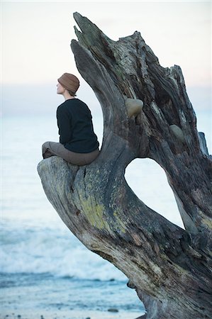 Woman sitting looking out from large driftwood tree trunk on beach Stock Photo - Premium Royalty-Free, Code: 614-08201990