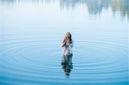 Young woman standing in lake ripples praying with eyes closed Stock Photo - Premium Royalty-Free, Code: 614-08202302