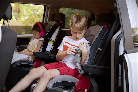 family inside car - Girl using digital tablet whilst brother fastens seat belt in car back seat Stock Photo - Premium Royalty-Free, Code: 614-08219860