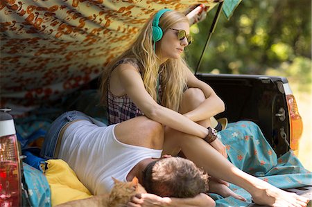 Young woman wearing headphones with boyfriend in pick up boot whilst camping Stock Photo - Premium Royalty-Free, Code: 614-08220143