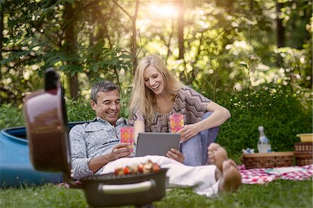 Mature man and girlfriend looking at digital tablet whilst having picnic barbecue Stock Photo - Premium Royalty-Free, Code: 614-08220151