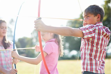 Girl practicing archery with teenage sister and brother Stock Photo - Premium Royalty-Free, Code: 614-08270380