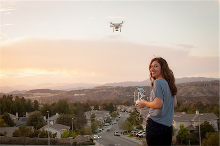 Female commercial operator flying drone above housing development, looking over shoulder at camera, Santa Clarita, California, USA Foto de stock - Sin royalties Premium, Código: 614-08308015