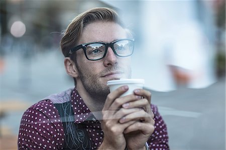 Sad young businessman behind city window drinking takeaway coffee Stock Photo - Premium Royalty-Free, Code: 614-08329527