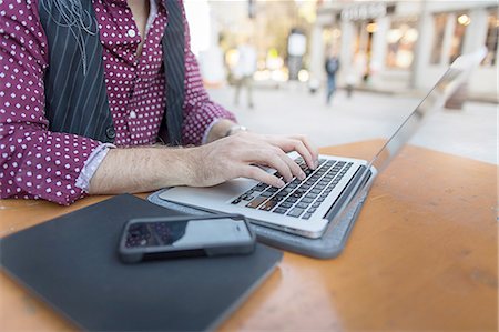 Cropped view of young businessman typing on laptop at sidewalk cafe Stock Photo - Premium Royalty-Free, Code: 614-08329521