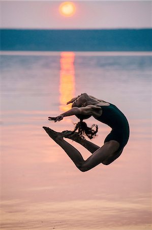 Side view of girl by ocean at sunset, leaping in mid air bending backwards Photographie de stock - Premium Libres de Droits, Code: 614-08383635