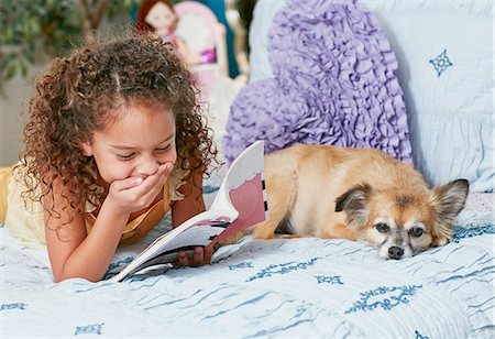 Girl and dog lying on bed reading book, hand on mouth laughing Foto de stock - Sin royalties Premium, Código: 614-08383722