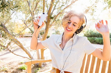 Mid adult woman sitting on bench, wearing headphones, holding smartphone, dancing Stock Photo - Premium Royalty-Free, Code: 614-08392351
