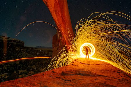 Silhouetted person creating yellow circular light trails on arch rock formation at night, Utah, USA Foto de stock - Sin royalties Premium, Código: 614-08392736