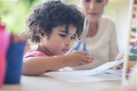 parents sitting with kids for crafts - Mother and son sitting at table, boy using scissors Stock Photo - Premium Royalty-Free, Code: 614-08578448