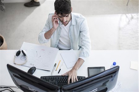 simsearch:649-06845199,k - Overhead view of male designer talking on smartphone whilst typing in design studio Stock Photo - Premium Royalty-Free, Code: 614-08641232