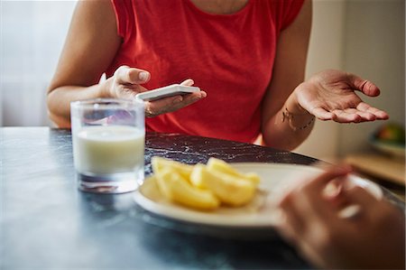 Cropped view of woman at dining table holding smartphone Stock Photo - Premium Royalty-Free, Code: 614-08721034