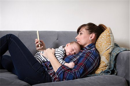 Mother with baby boy lying on sofa looking at smartphone Stock Photo - Premium Royalty-Free, Code: 614-08827186