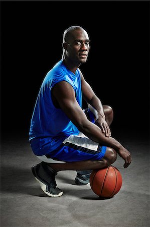 Studio portrait of basketball player kneeling on ball Stock Photo - Premium Royalty-Free, Code: 614-08875677