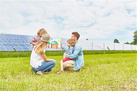 Young family sitting in field, looking at child's drawing of house, next to solar farm Stock Photo - Premium Royalty-Free, Code: 614-08877850