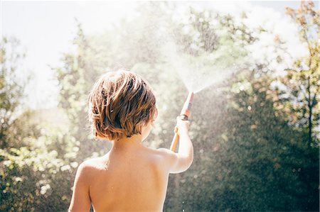 Low angle rear view of boy in garden spraying water from hosepipe, Bludenz, Vorarlberg, Austria Stock Photo - Premium Royalty-Free, Code: 614-08879277