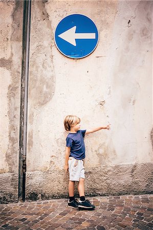 exploring children - Boy leaning against wall underneath direction sign pointing Stock Photo - Premium Royalty-Free, Code: 614-08879337