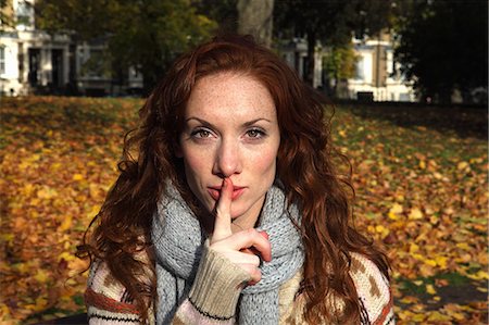 shhh - Woman holding finger over lips in park Stock Photo - Premium Royalty-Free, Code: 614-08870136