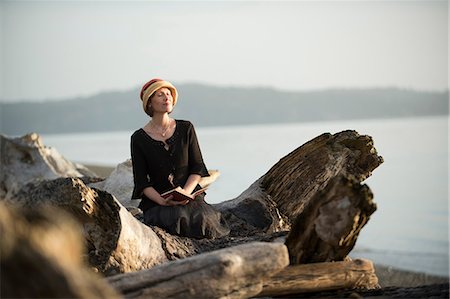 Woman sitting on driftwood Stock Photo - Premium Royalty-Free, Code: 614-08873980