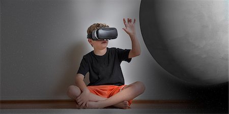 Young boy sitting cross legged, wearing virtual reality headset, reaching out to touch planet, digital composite Stock Photo - Premium Royalty-Free, Code: 614-08884611