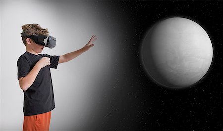 Young boy wearing virtual reality headset, reaching out to touch planet, digital composite Stock Photo - Premium Royalty-Free, Code: 614-08884612