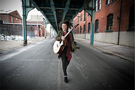 Young woman running below elevated road with acoustic guitar Stock Photo - Premium Royalty-Free, Code: 614-08885027