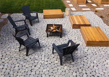 firepit and outdoors - Grey paving stone patio with black Adirondack sitting chairs, slightly raised flat rectangular red cedar wooden bench platforms around a metal firepit in residential backyard in summer, Quebec, Canada Stock Photo - Premium Royalty-Free, Code: 614-08881128